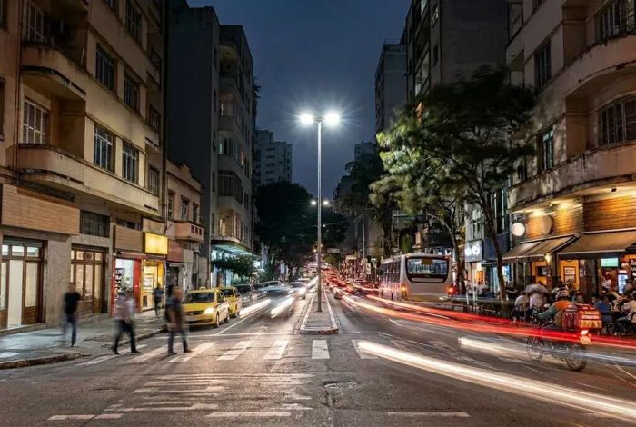 Uma rua vibrante à noite, com rastros de luz e prédios residenciais, em Santa Cecília em São Paulo.