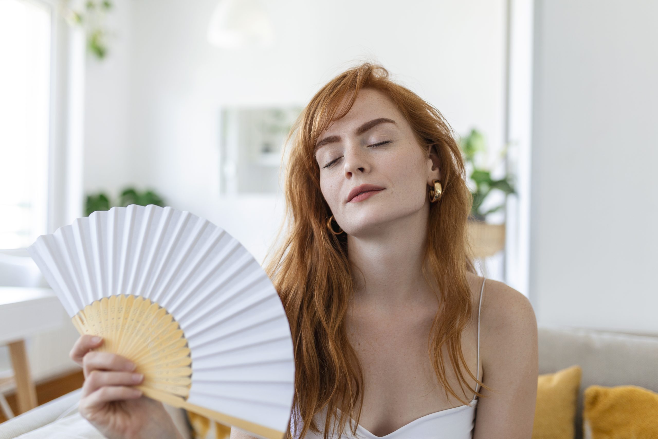 Mulher ruiva com calor se abannando com um leque. Ilustra o artigo sobre dicas de decoração para o verão