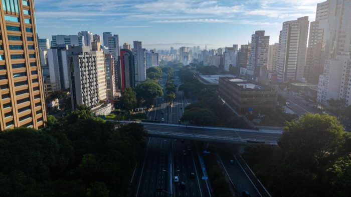 Avenida cercada por prédios altos e áreas verdes vista do alto, mostrando a paisagem moderna e urbana típica das zonas de São Paulo.