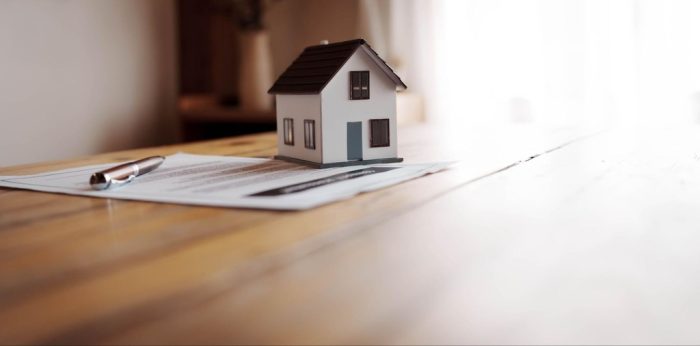 Miniatura de casa sobre documentos e caneta em mesa de madeira, ilustrando etapas e custos do registro de imóvel.