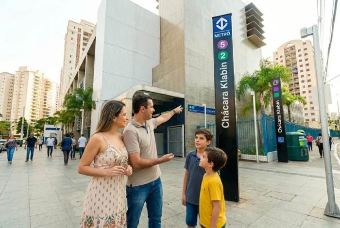 Família com duas crianças em frente ao totem de identificação da estação Chácara Klabin, ponto de conexão da linha lilás do metrô SP com a Linha 2-Verde.